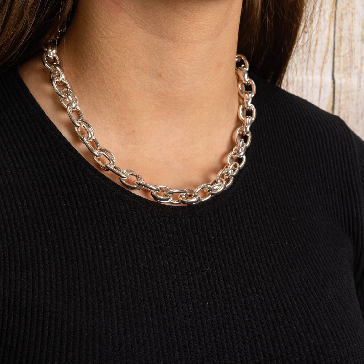 A close-up of a person wearing a chunky silver chain necklace with interlocking oval links, paired with a black ribbed top.