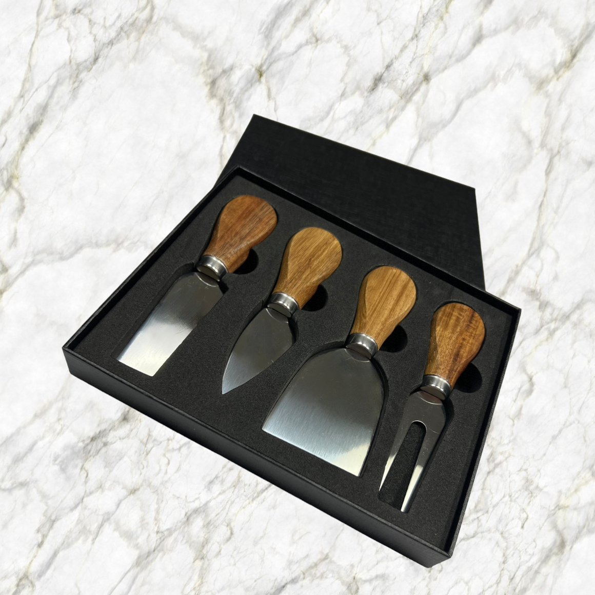 Set of four cheese tools with wooden handles in a black box on a marble background