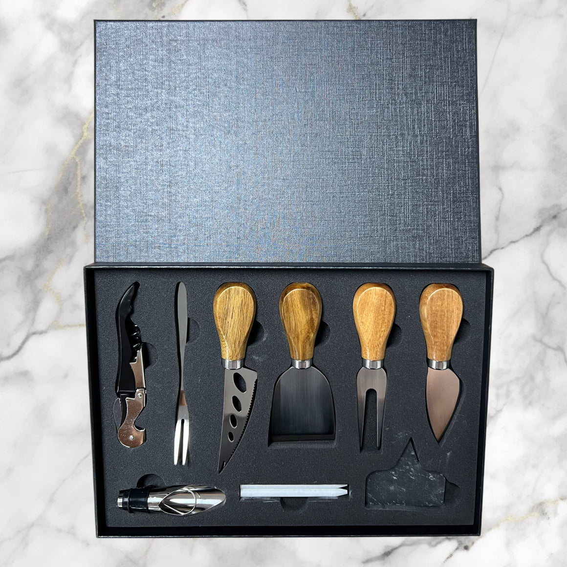 Set of cheese tools with wooden handles in a black box on a marble surface
