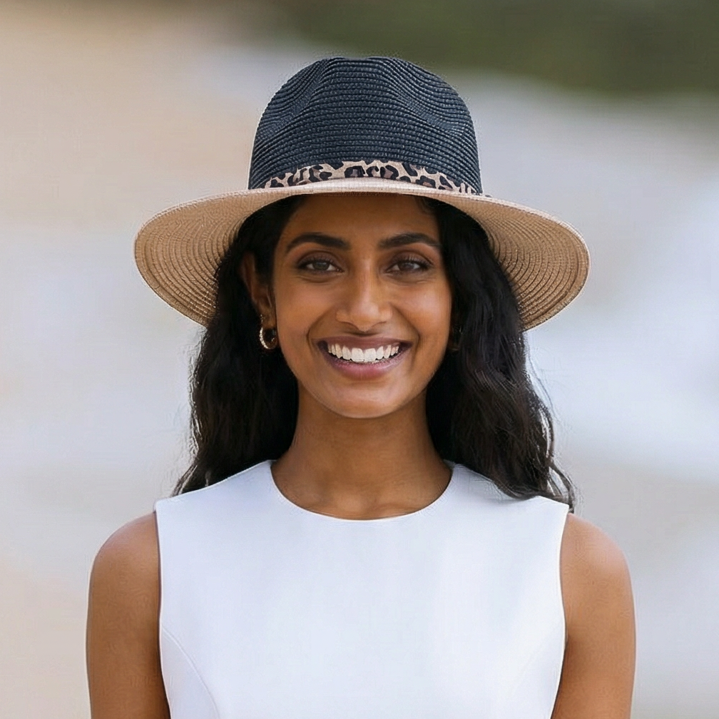 Woman wearing a straw hat with a leopard print band, smiling outdoors.
