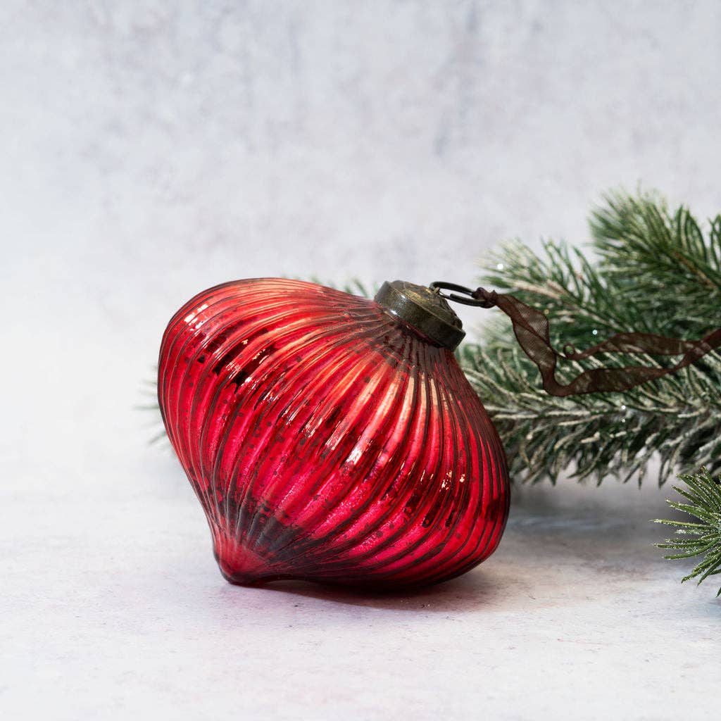 Red glass ornament with ribbed texture on a light gray background with a branch.