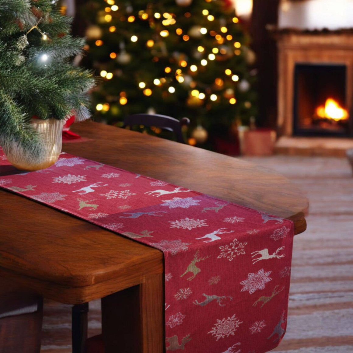 Red Christmas table runner with reindeer and snowflake pattern on a wooden table, blurred Christmas tree and fireplace in the background.