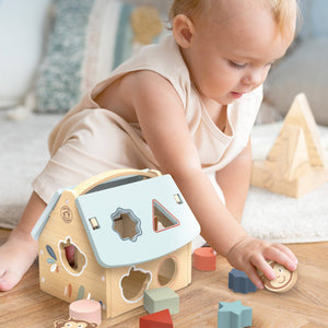 Baby playing with a shape sorter toy on a wooden floor.