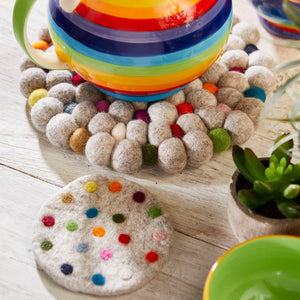 Colorful striped teapot on a decorative stand with a plant and coaster in the background.