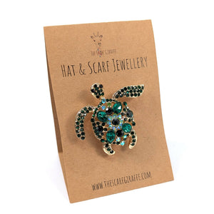 Tortoise-shaped brooch on a 'Hat & Scarf Jewellery' card with 'The Scarf Giraffe' branding.