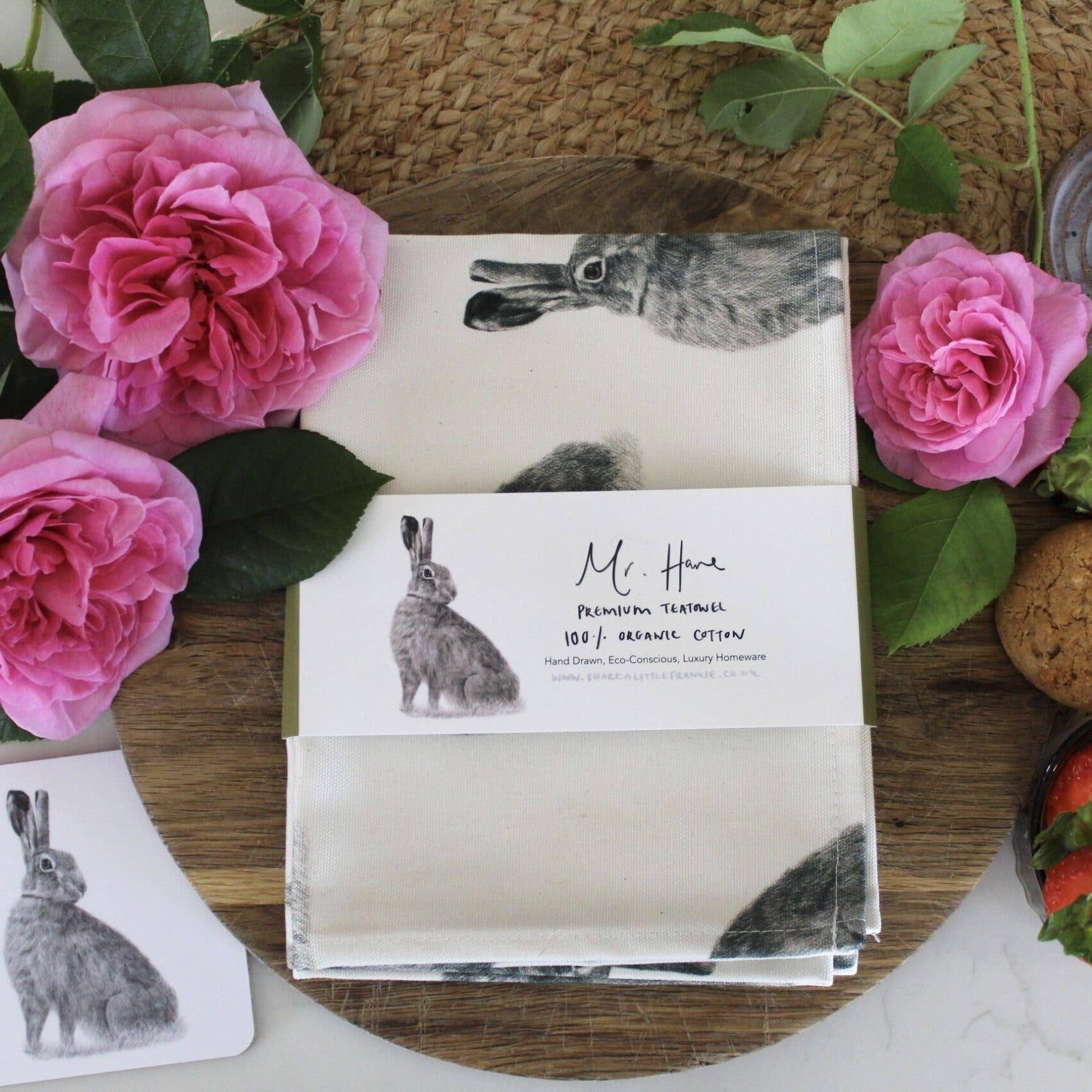 Table setting with pink roses, rabbit illustrations, and a napkin on a wooden board.
