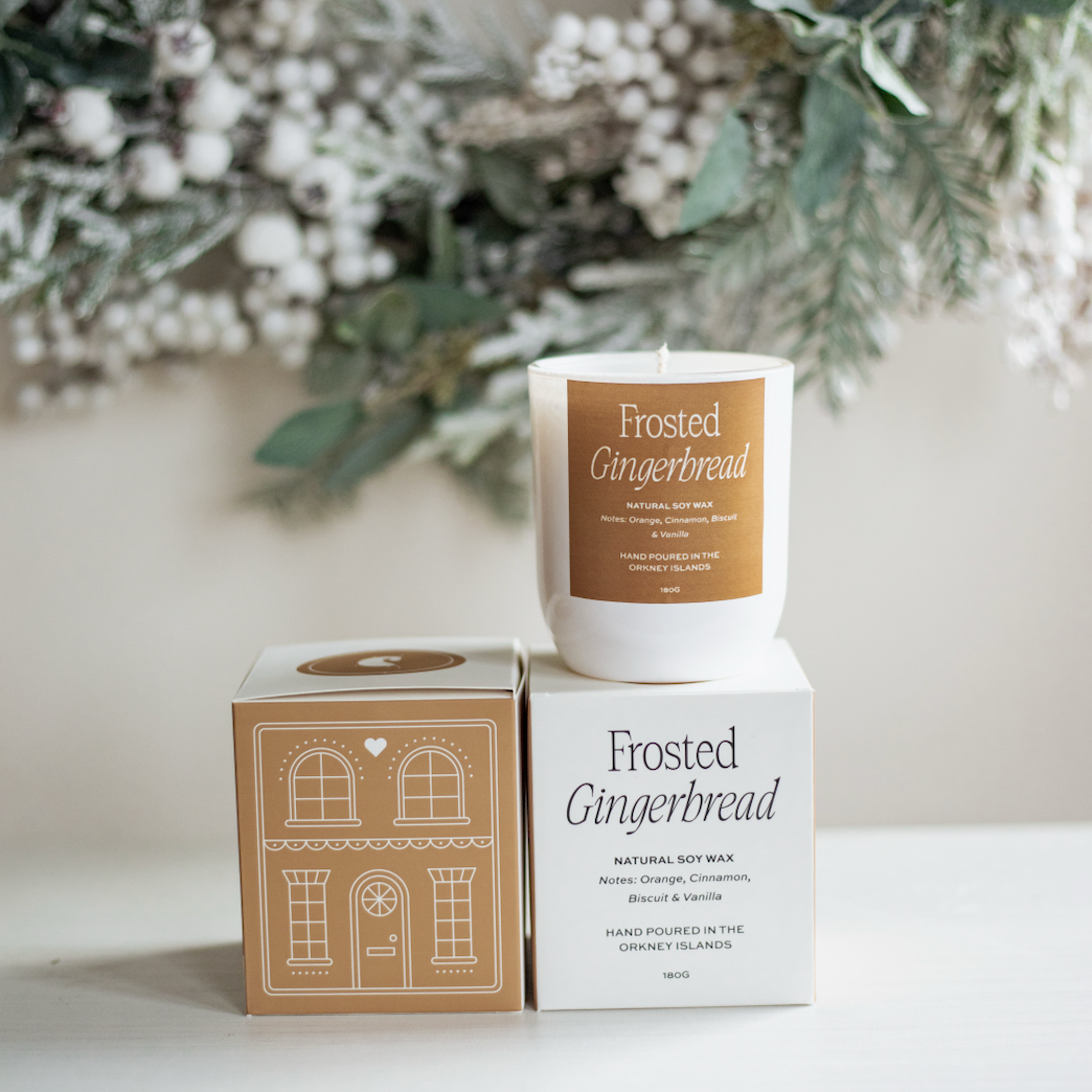 Frosted Gingerbread candle with packaging on a surface with decorative elements in the background