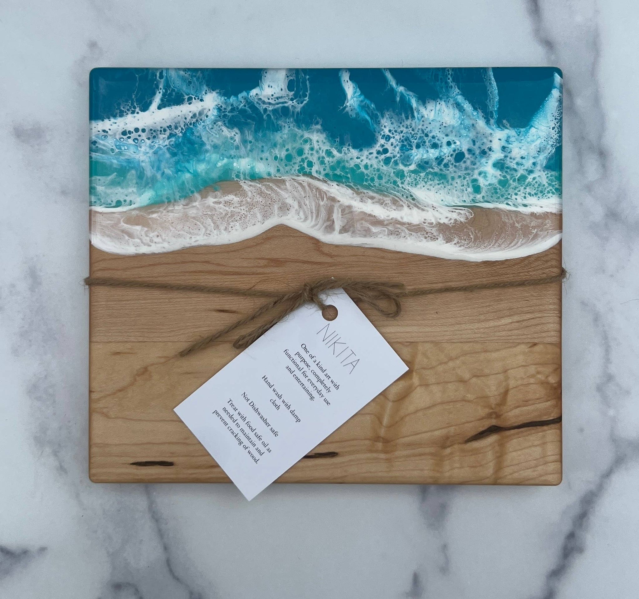 Wooden cutting board with ocean design and 'Nikita' tag on a marble background