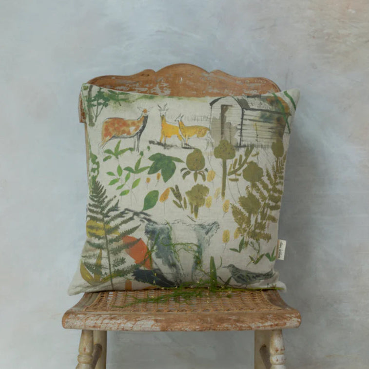 A square-shaped cushion with a nature and wildlife theme, featuring birds and foliage, placed on a neutral-toned sofa.