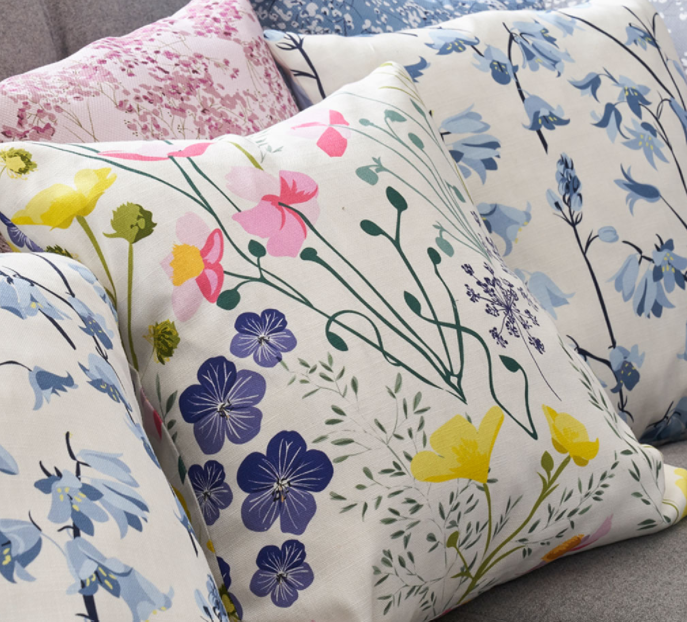 A collection of floral patterned cushions in various colors, featuring different flowers and foliage, arranged on a sofa.
