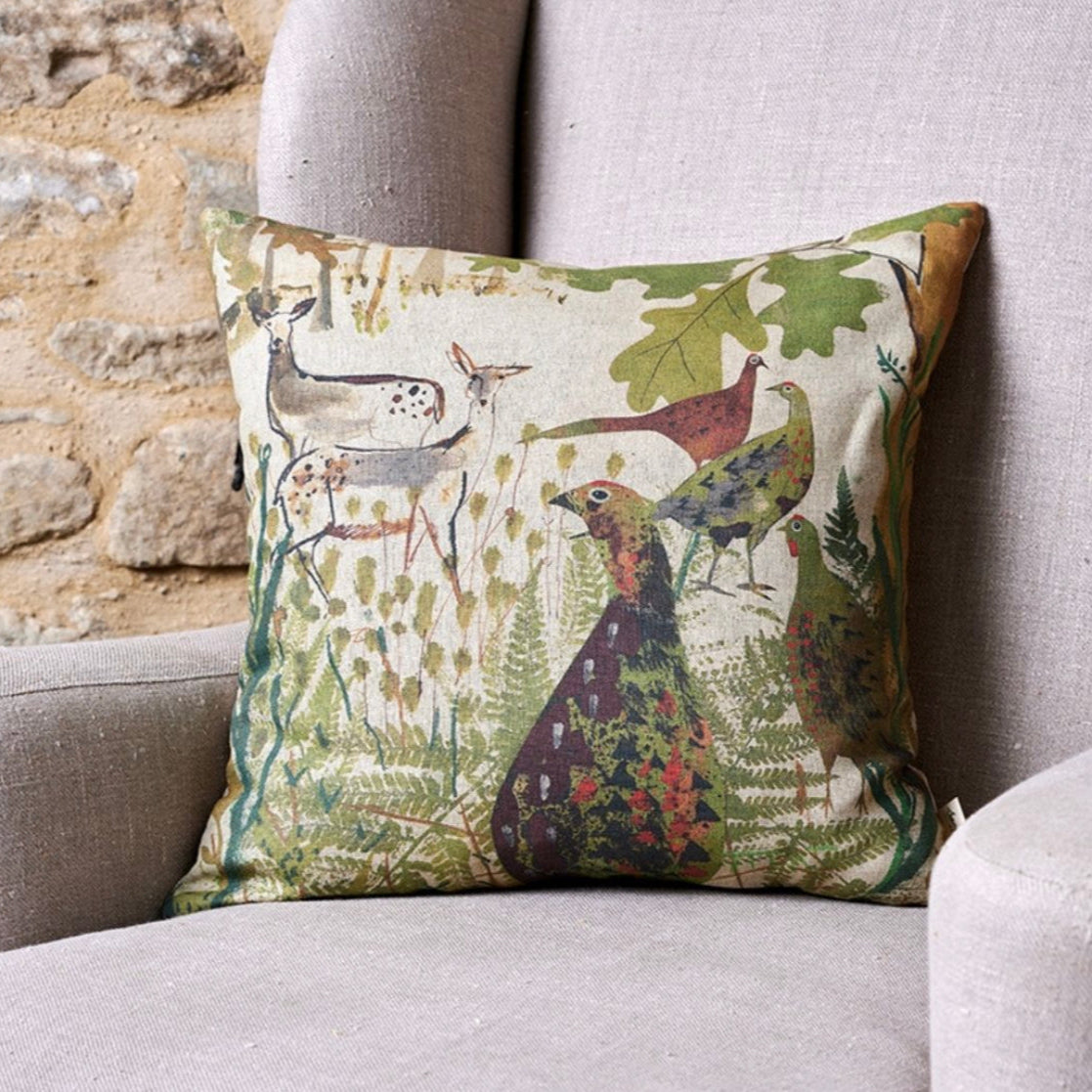 A square-shaped cushion with a nature and wildlife theme, featuring birds and foliage, placed on a neutral-toned sofa.